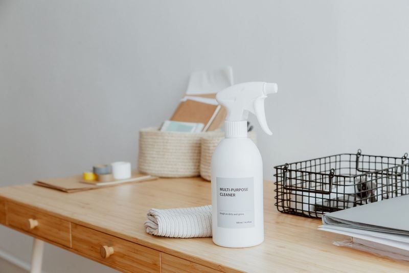 White spray bottle and a folded cloth on a tidy wooden desk